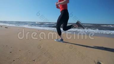 一个年轻女孩穿着红色运动服沿着海滩奔跑。 听耳机上的音乐。 晚上或早上慢跑表演